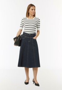 Gestreifter weißer und schwarzer Strickoberteil, kombiniert mit einem dunkelblauen Jeans-Midirock, das über vordere Taschen, genähte Details und eine ausgestellte Silhouette verfügt.