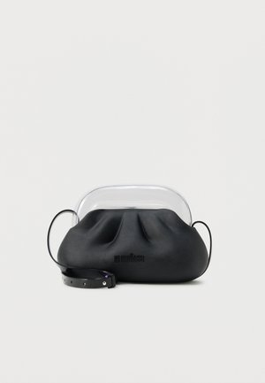 Fekete, puha bőrből készült kézitáska átlátszó műanyag felső fogantyúval és fekete, állítható vállpánttal, fehér felületen pihenve.