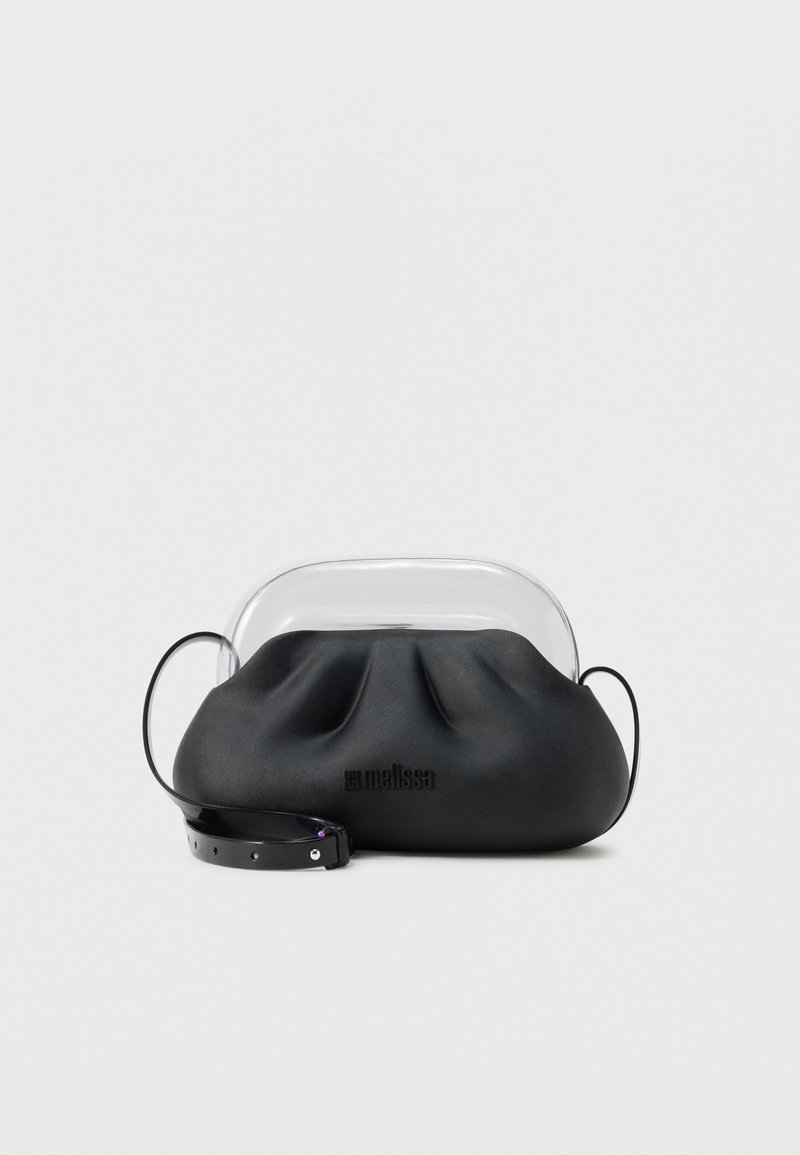 Μαύρη τσάντα ώμου από μαλακό δέρμα με διάφανο πλαστικό χειρολαβή στο πάνω μέρος και μαύρο ιμάντα ώμου με ρυθμιζόμενο μέγεθος, τοποθετημένη πάνω σε λευκή επιφάνεια.