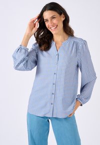 Blusa a scacchi blu e bianca con chiusura a bottoni, maniche lunghe a palloncino e colletto alla mandarino, realizzata in un tessuto leggero.