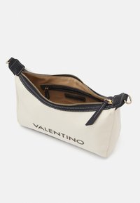 Kremfärgad canvasväska med svarta läderdetaljer, dragkedjestängning och sydda detaljer. Har en innerficka och "VALENTINO"-logotyp tryckt på framsidan.