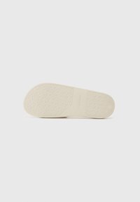 Off-white gummisole med et teksturert mønster som viser gjentatte sirkulære logoer. Glatt overflate langs kantene, minimal merking synlig.