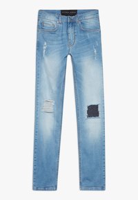 Jeans de un azul claro con corte ajustado, parches desgastados y detalles rasgados. Diseño clásico de cinco bolsillos con una cinturilla de altura media.