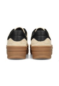 Sneaker in suede beige con tallone in pelle nera testurizzata, con suole di gomma a strati di colore marrone. Accenti curvi distintivi sul retro.