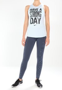 Top sin mangas de color azul claro con el texto "TENGA UN DÍA FUERTE", combinado con leggings azul oscuro que presentan un logo de Nike y líneas de acento blancas.