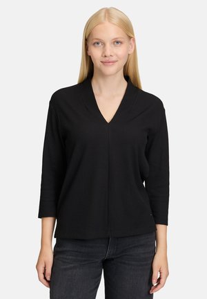 Zwarte V-hals pullover met een geribbelde textuur en driekwartmouwen, gedragen over donkere jeans. Eenvoudig, minimalistisch ontwerp.