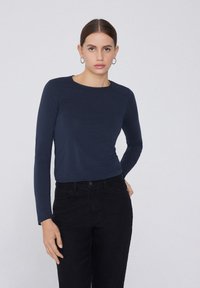Camiseta de manga larga azul marino de tela suave con cuello redondo, combinada con vaqueros negros de cintura alta. Diseño simple, sin patrones ni acentos visibles.