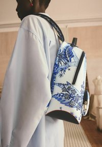 Mochila de patrón azul y blanco hecha de material sintético suave, con un compartimento con cremallera y una correa negra.