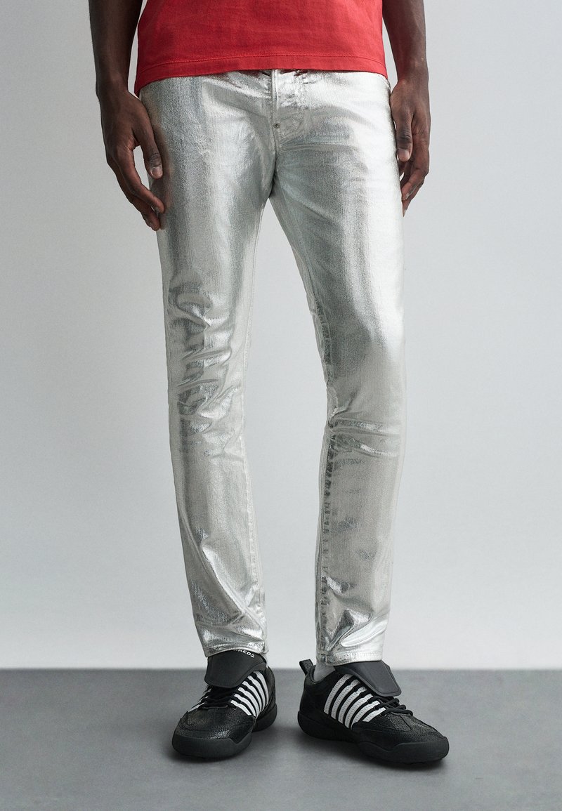 Hõbedased metallik teksad, millel on kitsas lõige ja sile tekstuur. Kombineeritud musta ja valge triibuliste tossudega, rõhutades sportlikku disaini.