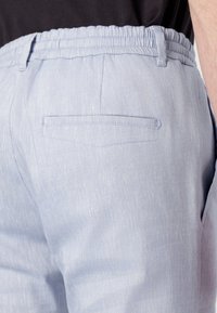 Lys blå, teksturerte bukser med elastisk midjebånd, som har en enkelt baklomme og subtile sømdetaljer.