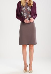 Violetti neuletakki kuvioidun kukkakuosisen topin päällä, yhdistettynä istuvaan harmaaseen mekkoon ja kultaisiin korkokenkiin.