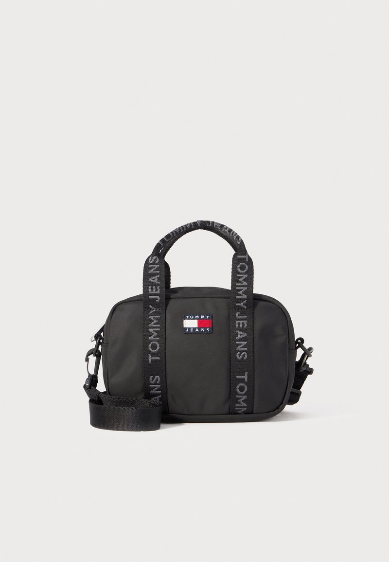 Zwarte nylon handtas met een rechthoekige vorm, voorzien van dubbele handvatten aan de bovenkant en een afneembare schouderband. De voorkant toont een kleurrijke logopatch.