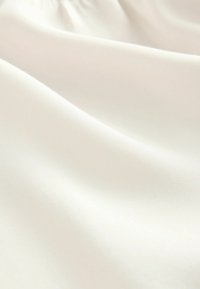 Crème-kleurige stof met een gladde, glanzende textuur, voorzien van subtiele ribstructuren. Het materiaal lijkt licht en vloeiend.