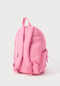 Zaino rosa con spallacci imbottiti, chiusura con zip e tasche laterali. Il tessuto è liscio, con un design semplice e una maniglia superiore per il trasporto.