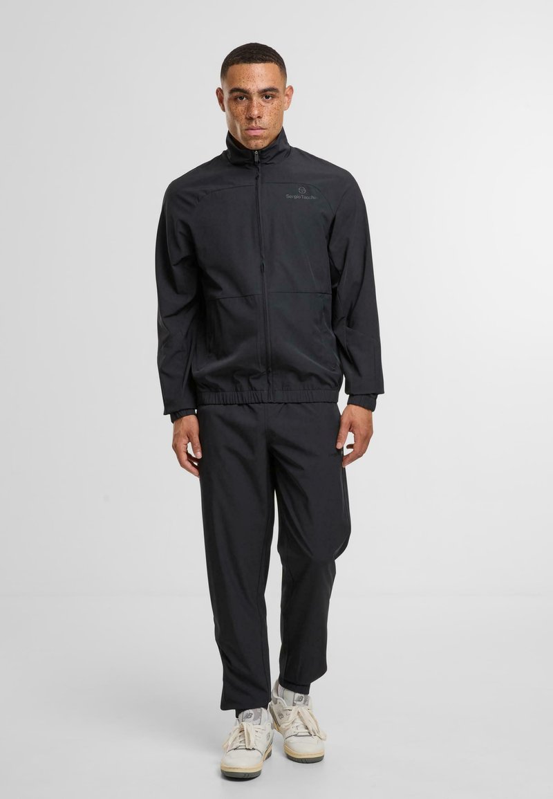 Černá lehká bunda se zipem a stojáčkem, spárovaná s úzkými kalhotami ve stejně barevném provedení. Obsahuje elastické manžety a pas.