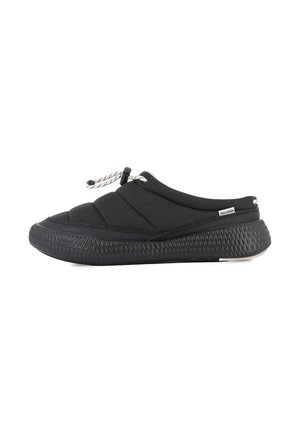 Zapatilla deportiva negra tipo slip-on con suela gruesa y texturizada, parte superior acolchada, cordón blanco y etiqueta de la marca Palladium en el lateral y la suela.