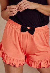 Koralowe bawełniane szorty z falbanką na dole i czarną kokardą na pasku; noszone z czarnym topem.