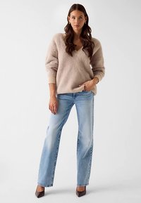 Light beige, oversized sweater with a V-neck and ribbed cuffs, paired with straight-leg light blue jeans and dark brown heels.
