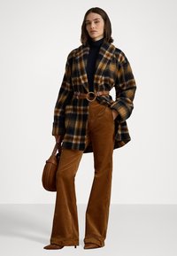 Cappotto scozzese in nero, arancione e giallo con vestibilità over. Pantaloni in velluto a coste marroni. Cintura marrone con anello in metallo e borsa abbinata.