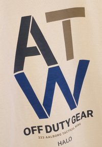 Kremowy materiał wyróżnia się wyrazistym niebieskim i czarnym geometrycznym tekstem, z detalami "OFF DUTY GEAR" oraz "223 AALBORG TACTICAL WING" w kolorze czarnym.