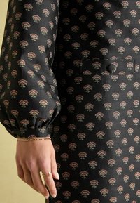 Schwarzes Kleid aus Stoff mit einem sich wiederholenden Blumenmuster in Rosa- und Grautönen. Puffärmel, ein Knopfverschluss und eine Seitentasche.