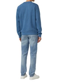 Niebieski sweter typu pulower o teksturowanym wzorze dzianiny, zestawiony z jasnymi dżinsami i białymi sneakersami. Sweter jest wyposażony w prążkowany dół i mankiety.