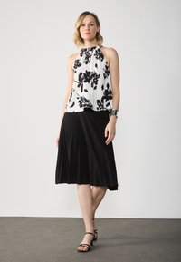 Lillelillelise floralne top must-valge, koos musta volditud midi seelikuga. Mudel kannab musti rihmadega kontsi. Üksik taust.