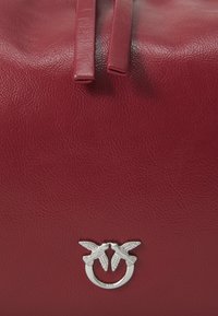Red leather bag with two matching straps and a silver ring featuring two birds facing each other at the center.