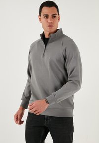 Šedý svetr s širokým zipem, žebrovanými manžetami a diskrétním logem. Hladká textura; mírně přiléhavý střih.