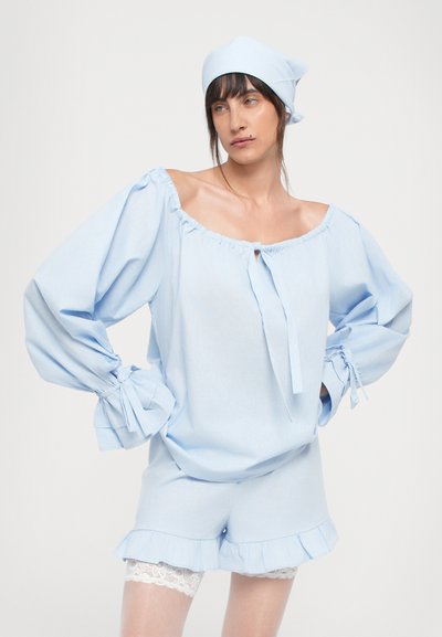 Blouse bleu clair à épaules dénudées avec des manches surdimensionnées et des poignets noués, assortie à un short avec des ourlets volants et une finition en dentelle.