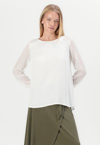 Weißes Oberteil mit strukturierten, transparenten, chevron-musterlongsleeves. Verfügt über einen runden Halsausschnitt und eine lockere Passform, kombiniert mit einem olivgrünen Rock.