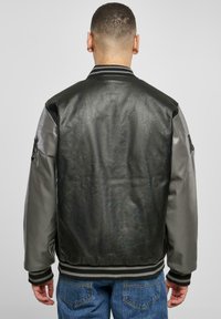 Black leather bomber jacket with grey sleeves, ribbed collar and cuffs, and back pocket detail. Smooth texture, fitted design.