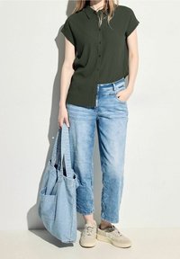 Tmavě zelená košile s krátkým rukávem na knoflíky, světle modré volné džíny, světle modrá taška přes rameno a béžové tenisky s texturovanými detaily.