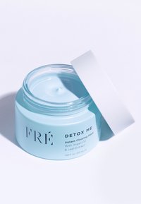Jasnoniebieski słoik oznaczony etykietą "FRÉ DETOX ME Instant Clearing Mask", z białą pokrywką. Zawartość wydaje się kremowa i gładka wewnątrz przezroczystego pojemnika.