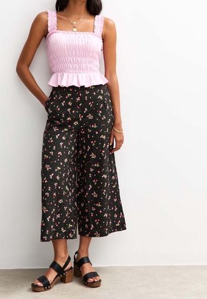 Pink smocked peplum top with ruffled straps, paired with black cropped pants featuring small floral print. Black chunky heeled sandals.