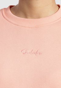Lichtroze sweatshirt met een geribde ronde hals en geborduurd "Smilodon"-label in bijpassend roze. Gladde stofstructuur.