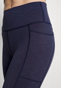 Mörkblå leggings i texturerat tyg, med hög midja och platta sömmar. Sidficka integrerad i designen.