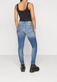 Jeans ajustados de color azul con un acabado desgastado, que cuentan con una cintura alta, mínimo hardware y bolsillos traseros. Combinados con botas militares negras.