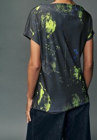 Černý krátký rukáv top s abstraktním vzorem v zelené a modré. Volný střih s širokým výstřihem a měkkou tkaninou. Nosit s tmavou denim.