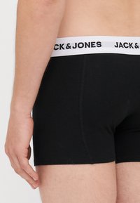 Schwarze Baumwollboxershorts mit einem weißen elastischen Bündchen, auf dem der Markenname "JACK & JONES" in schwarzer Schrift zu sehen ist.