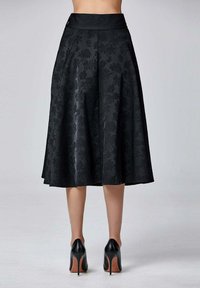 Jupe noire midi avec un motif floral, taille haute et silhouette fluide, associée à des chaussures à talons hauts noires. Texture lisse, éclat minimal.