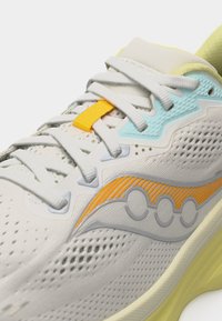 Λευκό και παστέλ κίτρινο αθλητικό παπούτσι με πλέγμα επάνω μέρος, λευκά κορδόνια, ανοιχτό μπλε και πορτοκαλί λεπτομέρειες, και μαλακή σόλα.