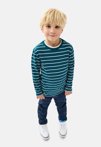 Vaaleansininen raidallinen pitkähihaisvaate, jossa on valkoisia vaakaraitoja, yhdistettynä farkkuihin ja valkoisiin tennareihin, joissa on sinisiä yksityiskohtia.