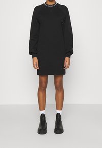 Svart sweatshirtklänning med rund halsringning och långa puffärmar. Har en krage med logotyp och en avslappnad passform. Bärs med ankellängda stövlar.