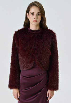 Giacca cropped in pelliccia sintetica bordeaux con maniche lunghe, caratterizzata da una texture morbida e un colletto rotondo, abbinata a un vestito in satin dello stesso colore.