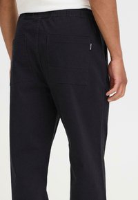 Pantalones de algodón negros con cintura elástica, bolsillos laterales y dos grandes bolsillos traseros con una textura suave.
