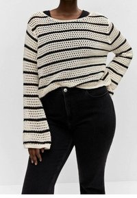 Jersey de punto con un patrón de rayas en crema y negro, con un diseño de tejido abierto y mangas largas y anchas, combinado con unos vaqueros negros.