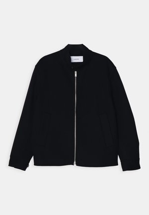 Mustamüts, millel on püsti krae, ees lukuga sulgemine ja kaks küljetaskut. Valmistatud siledast kangast, millel on soonikkoes varrukad.