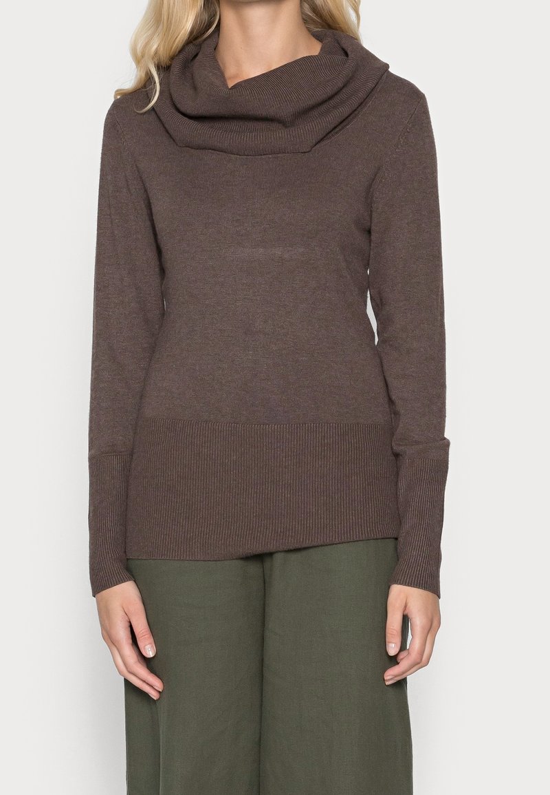 Brązowy sweter z kołnierzem typu cowl, z długimi rękawami, struktura ściągaczy u dołu i przy mankietach, w zestawie z luźnymi zielonymi spodniami.
