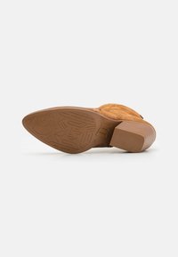 Bota de tobillo de ante marrón con un tacón grueso, que cuenta con una suela de goma texturizada y un intrincado diseño de banda de rodadura para mejorar el agarre.